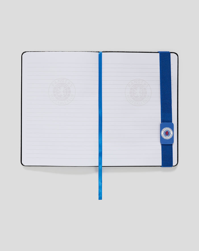 A5 notepad open with blue elastic band and blue ribbon bookmark on lined pages with a faint crest watermark.