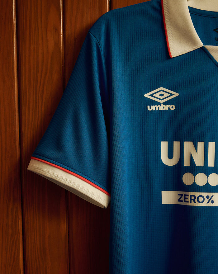 Close up of blue Rangers home shirt chest area showing ribbed knit and sleeve with white cuff and red piping.