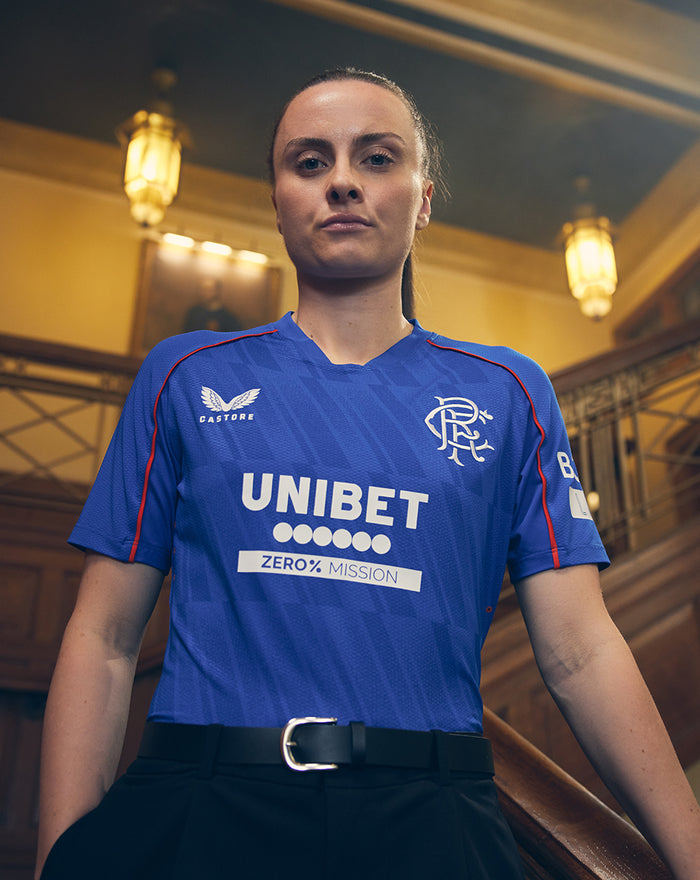 Portrait of a woman wearing a blue Rangers Pro Home shirt with UNIBET sponsor in an indoor staircase setting