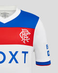 Close up of Rangers junior away shirt showing blue shoulder panel and red chest stripe with white crest on white fabric.