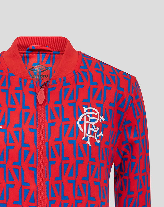 Close-up of junior away jacket showing red and blue geometric pattern with crest on the left chest and center front zipper.