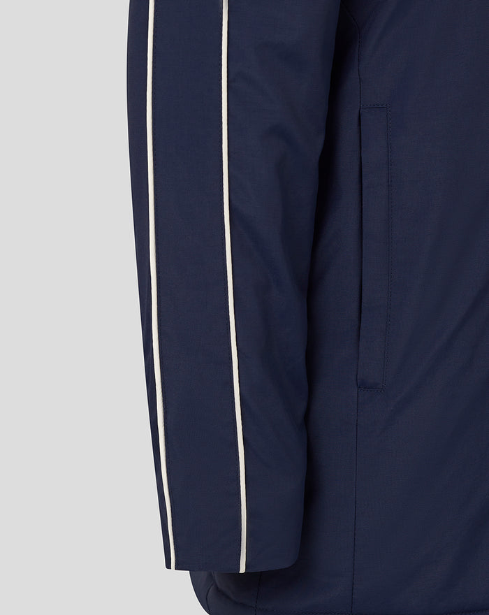 Side profile of navy Junior 25/26 Travel Bench Jacket showing white piping along the sleeve and a vertical pocket