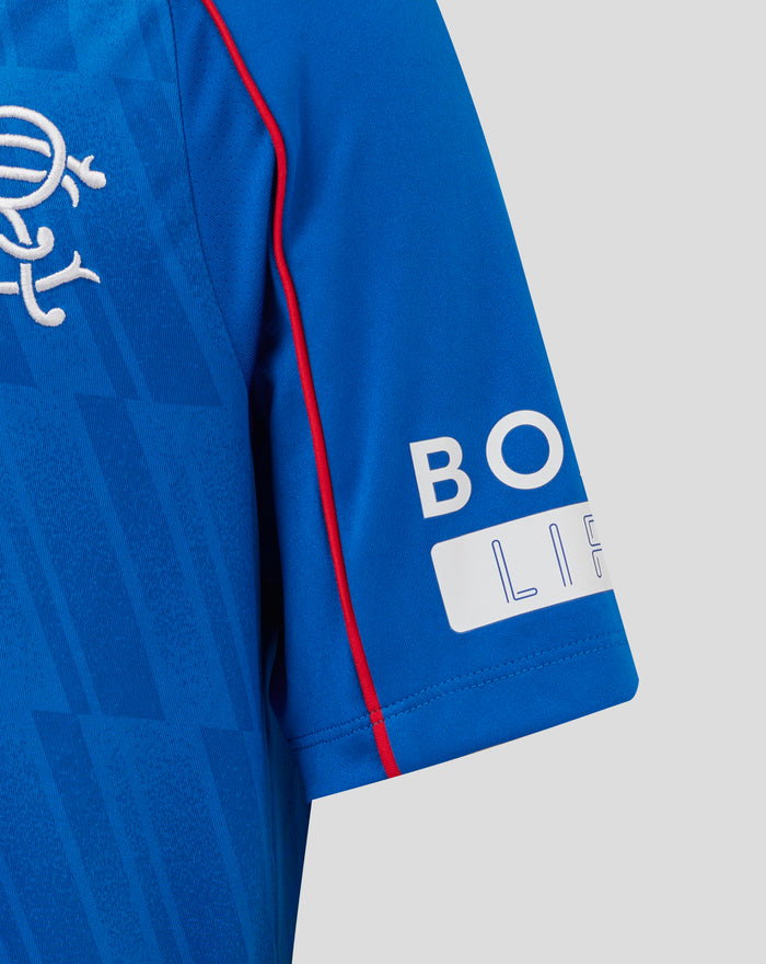 Close up of junior Rangers home shirt in blue with crest on the left chest and red piping along the sleeve seam