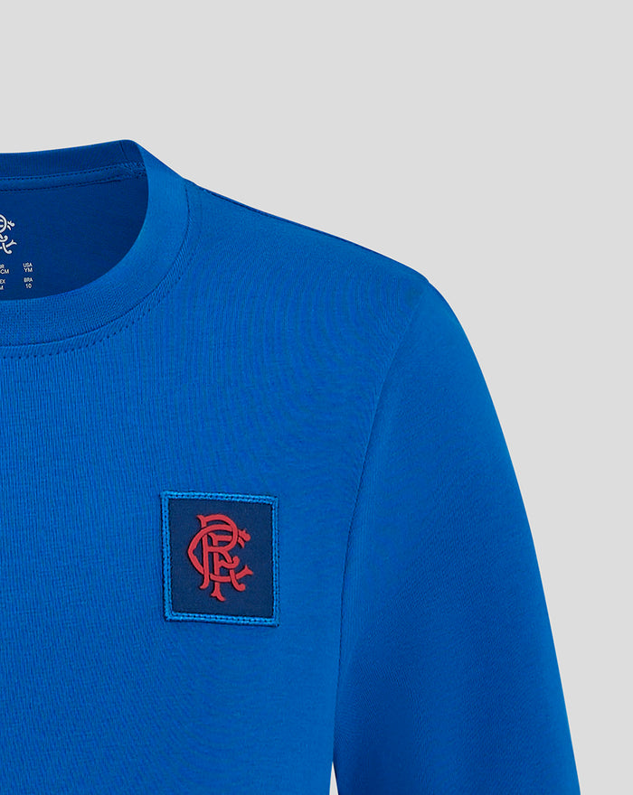 Close up of the blue T shirt chest area showing a red crest emblem on a dark square patch