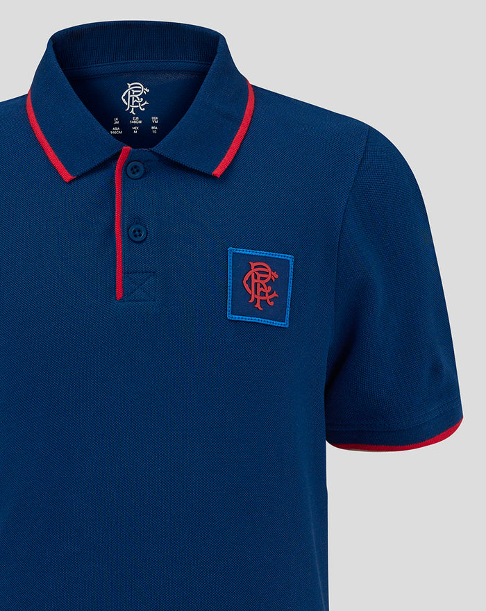 Close-up of navy junior polo showing red piping on the collar and a chest crest patch