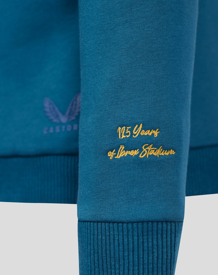 Close-up of blue sweatshirt front showing gold 125 Years embroidery near the hem.