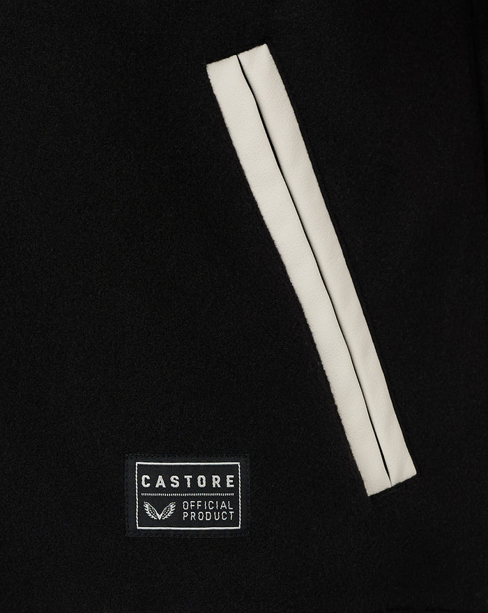 Close up of black varsity jacket pocket with white piping and Castore badge