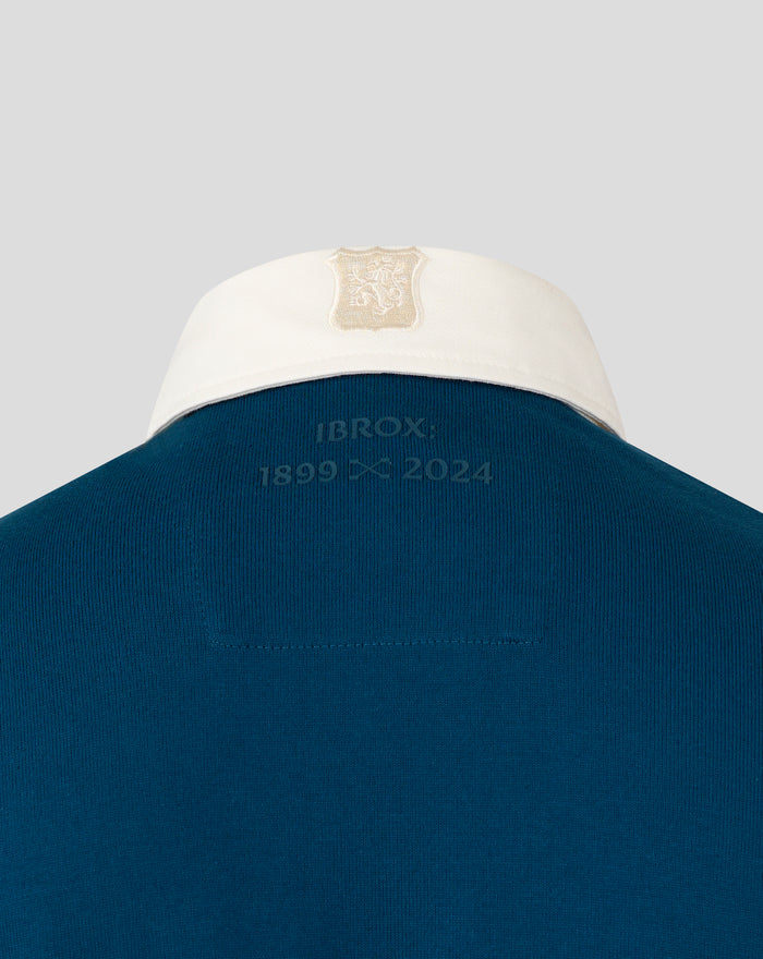 Back view of teal heritage polo with white collar and embroidered anniversary text at the neck.