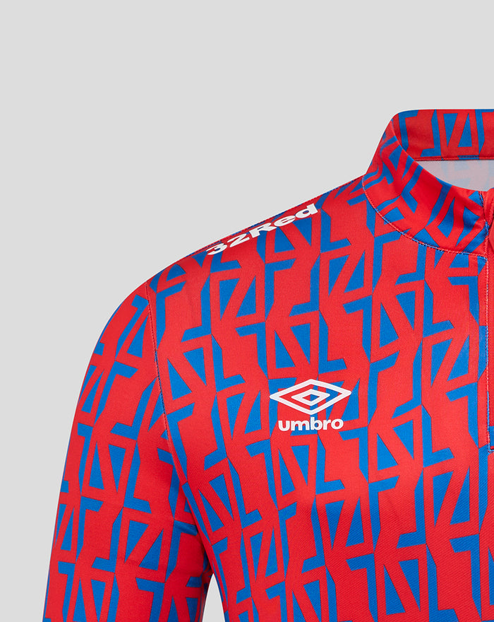 Close up of red away matchday quarter zip top with blue geometric pattern and Umbro logo on chest.
