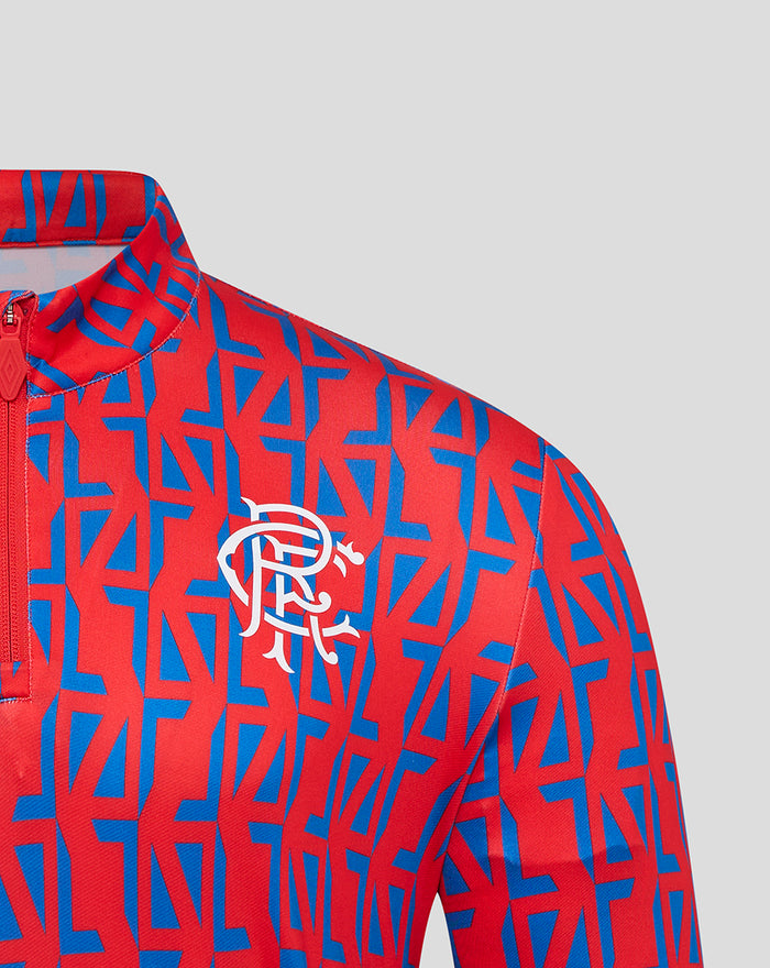Close up of the red and blue patterned quarter zip jersey showing the club crest and Umbro logo on the chest