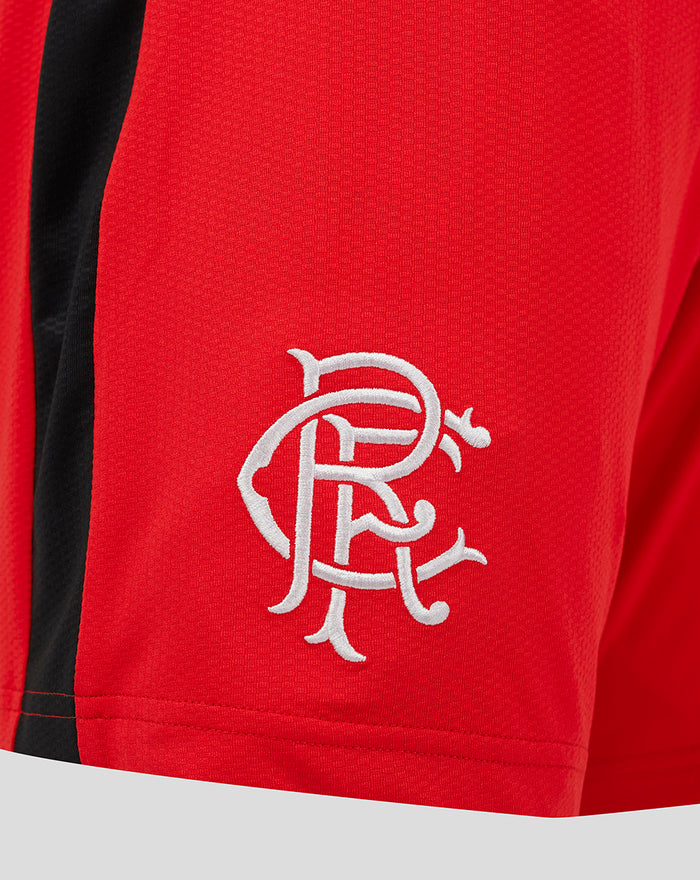 Close-up of white embroidered crest on red fabric shorts.