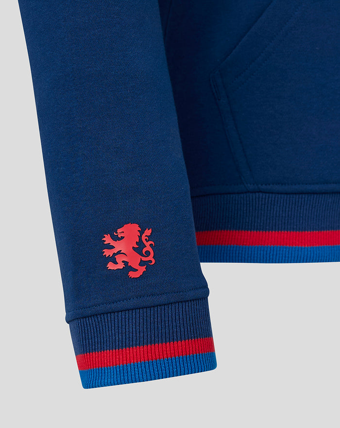 Close up of sleeve on blue hoodie showing a red crest logo near the cuff and a red blue striped ribbed cuff at the wrist