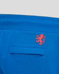 Close-up of blue shorts pocket area with a flap pocket and red crest above a red vertical stripe.