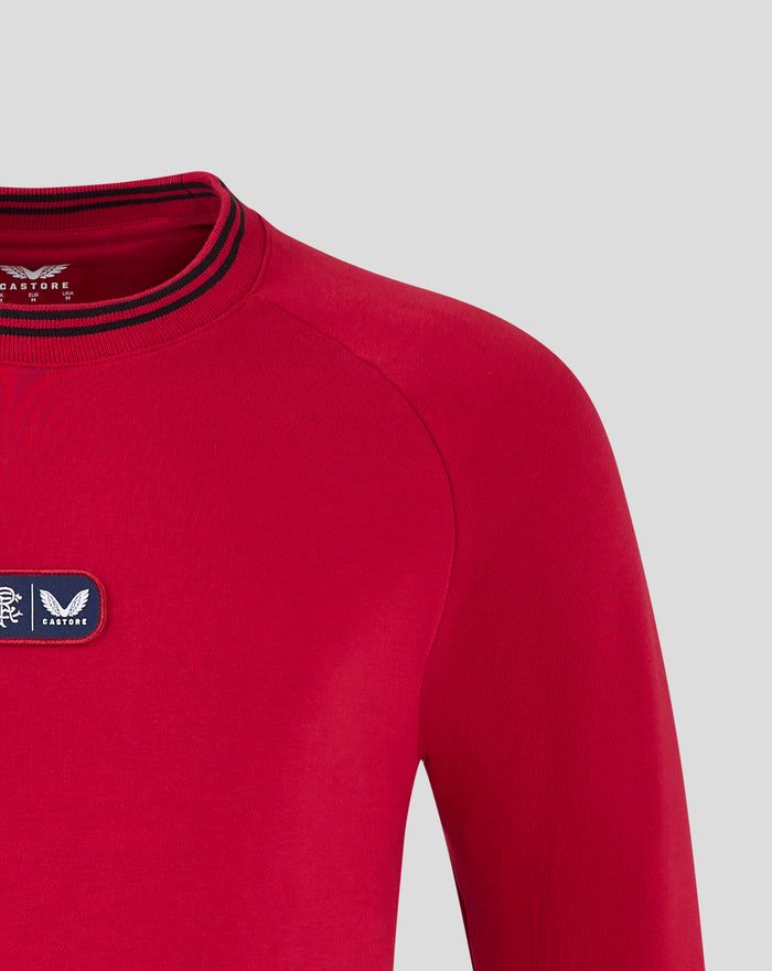 Detail view of red fleece crewneck showing shoulder seam and chest patch on the front left