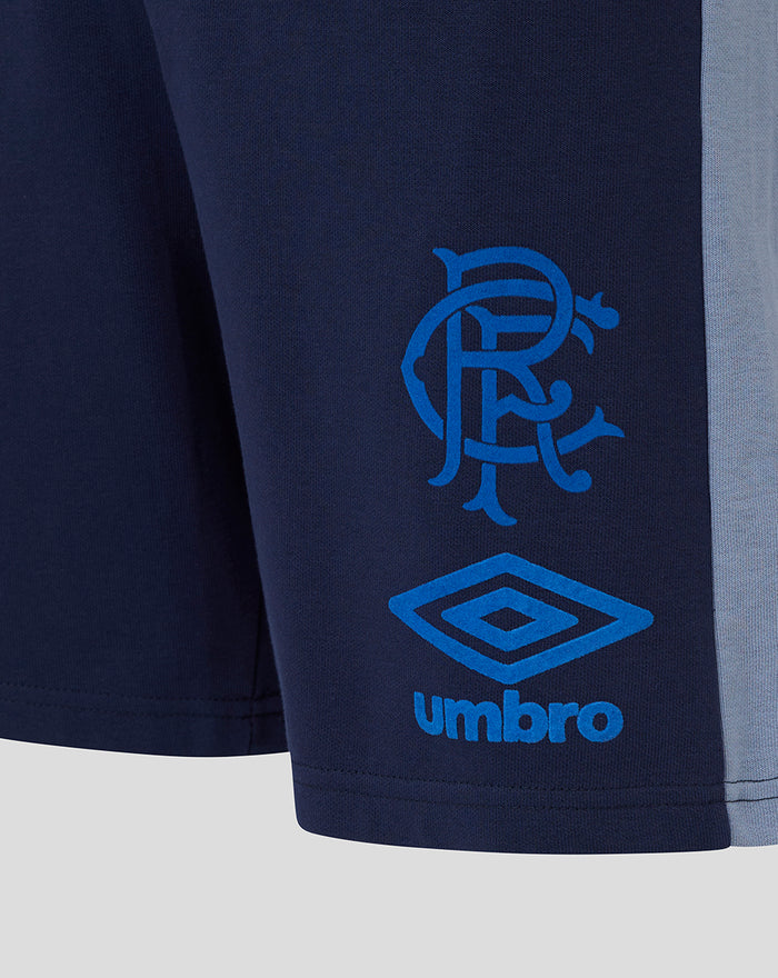 Side view of navy travel shorts showing a light blue side stripe and blue Castore logo and club crest near the hem.
