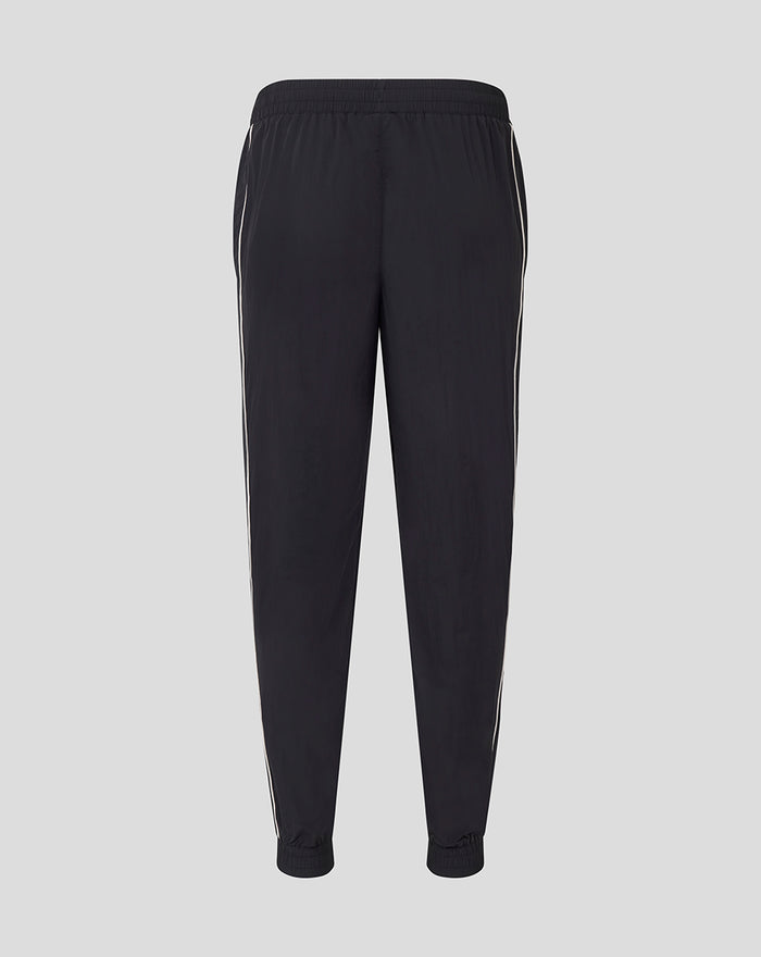 Detail of lower leg showing white piping and red club crest with Umbro logo on black travel pants
