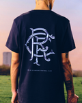 Back view of a navy t shirt worn by a person, featuring a large decorative intertwined RFC emblem on the back.