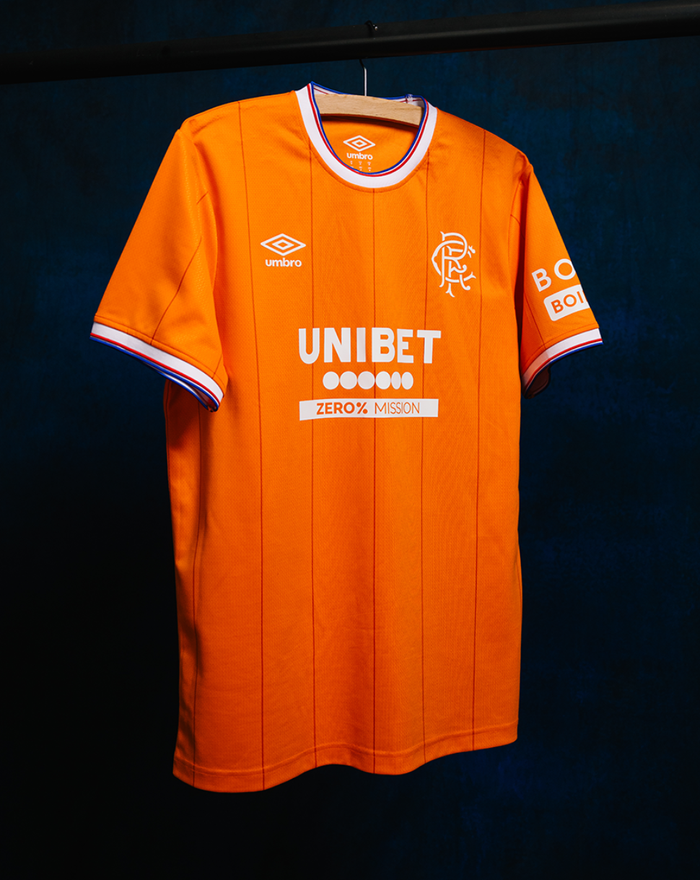 Orange Rangers FC replica shirt hanging on a wooden hanger against a dark backdrop showing Umbro logo and club crest