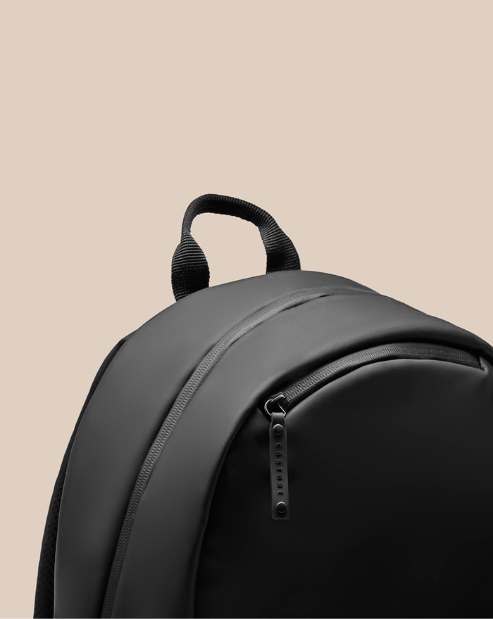 Close up of CORE BACKPACK top showing a grip handle and a CASTORE branded zipper pull.