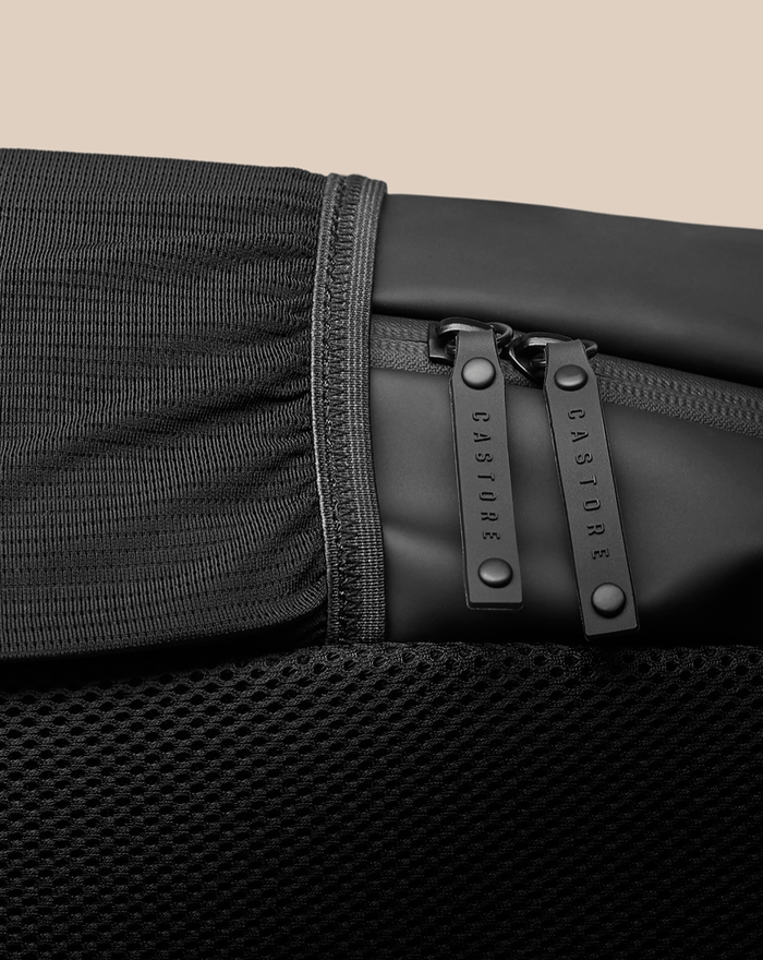 Close up of CORE BACKPACK zipper pulls and black fabric edge with branding