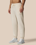 Beige cotton fleece joggers with drawstring waist and small logo on the thigh, paired with white sneakers.