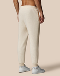 Back view of a model wearing beige cotton fleece joggers with an elastic waist and ribbed cuffs