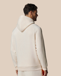 Back view of beige cotton fleece hoodie on a male model with the hood up against a pale tan backdrop