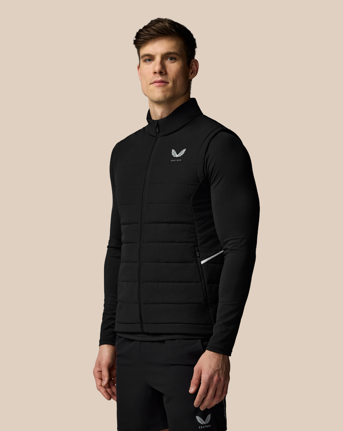 Male model wearing a black padded gilet with a zip front and small chest logo.