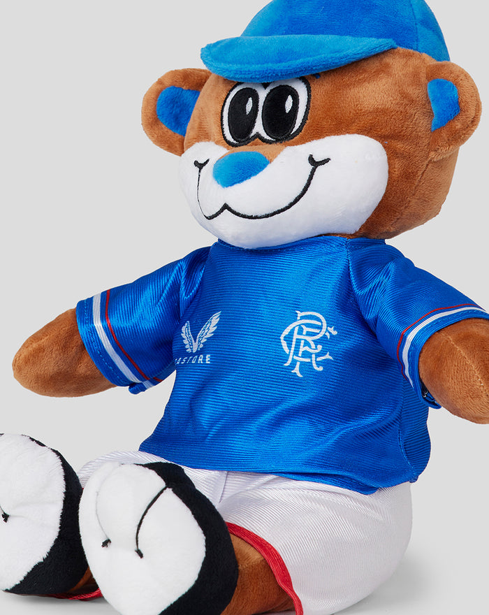 Close up of BROXI BEAR plush in a blue jersey with crest details and white shorts.